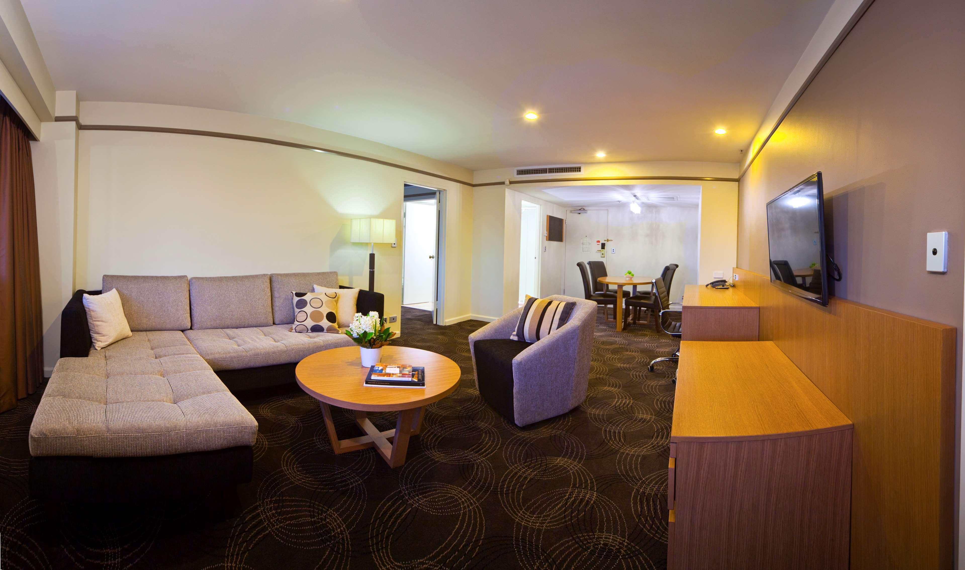 Stamford Plaza Adelaide Hotel Exterior foto The photo shows a spacious living area with modern decor. On the left, there is a light gray sectional sofa, accompanied by a round wooden coffee table in front of it. A couple of decorative pillows add a touch of color to the sofa. To the right, the