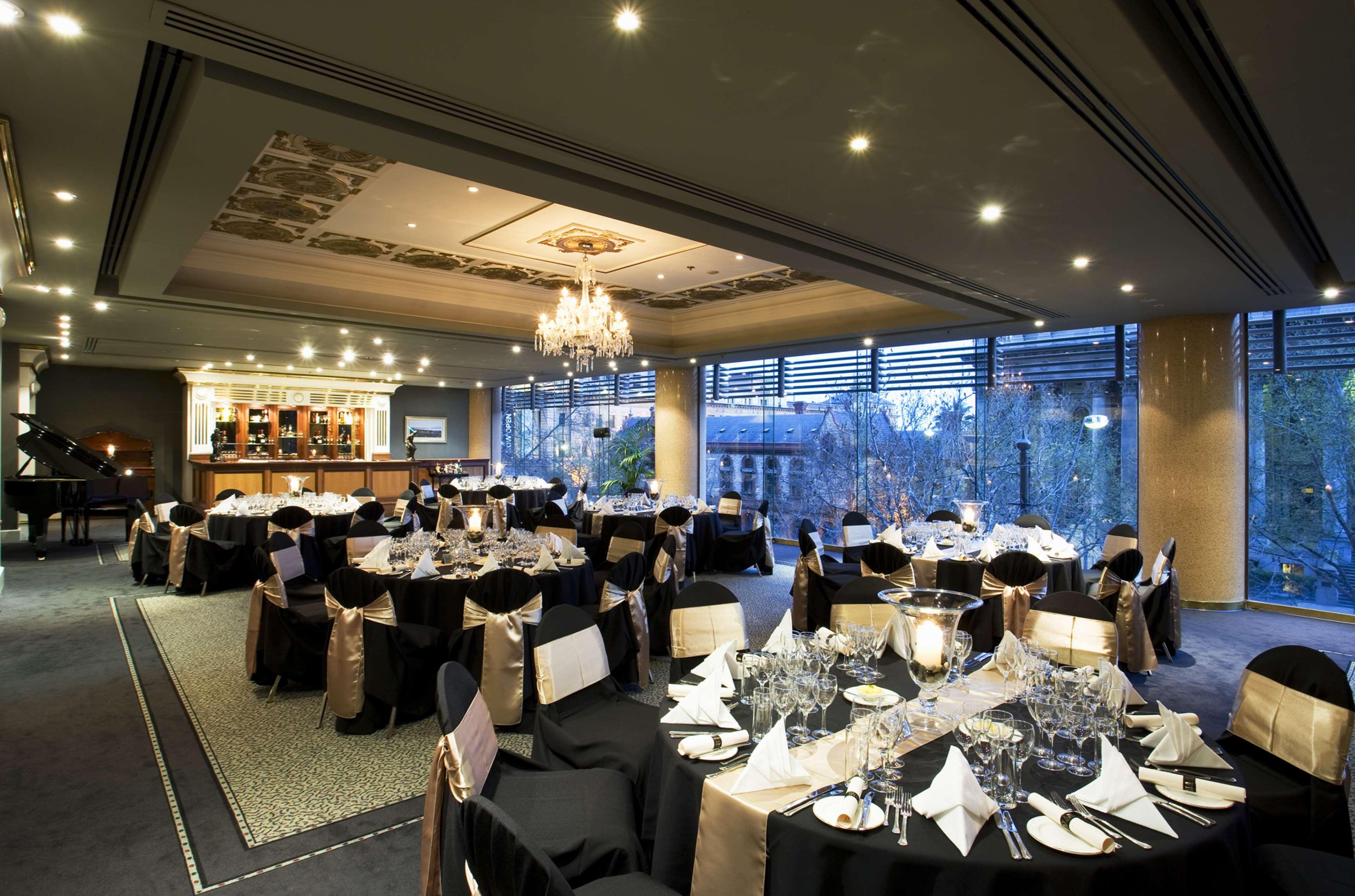 Stamford Plaza Adelaide Hotel Exterior foto The photo shows an elegant banquet hall or restaurant setting. There are several round tables covered with black tablecloths and adorned with gold accents. Each table is set with fine dining utensils, glassware, and neatly folded napkins. In the back