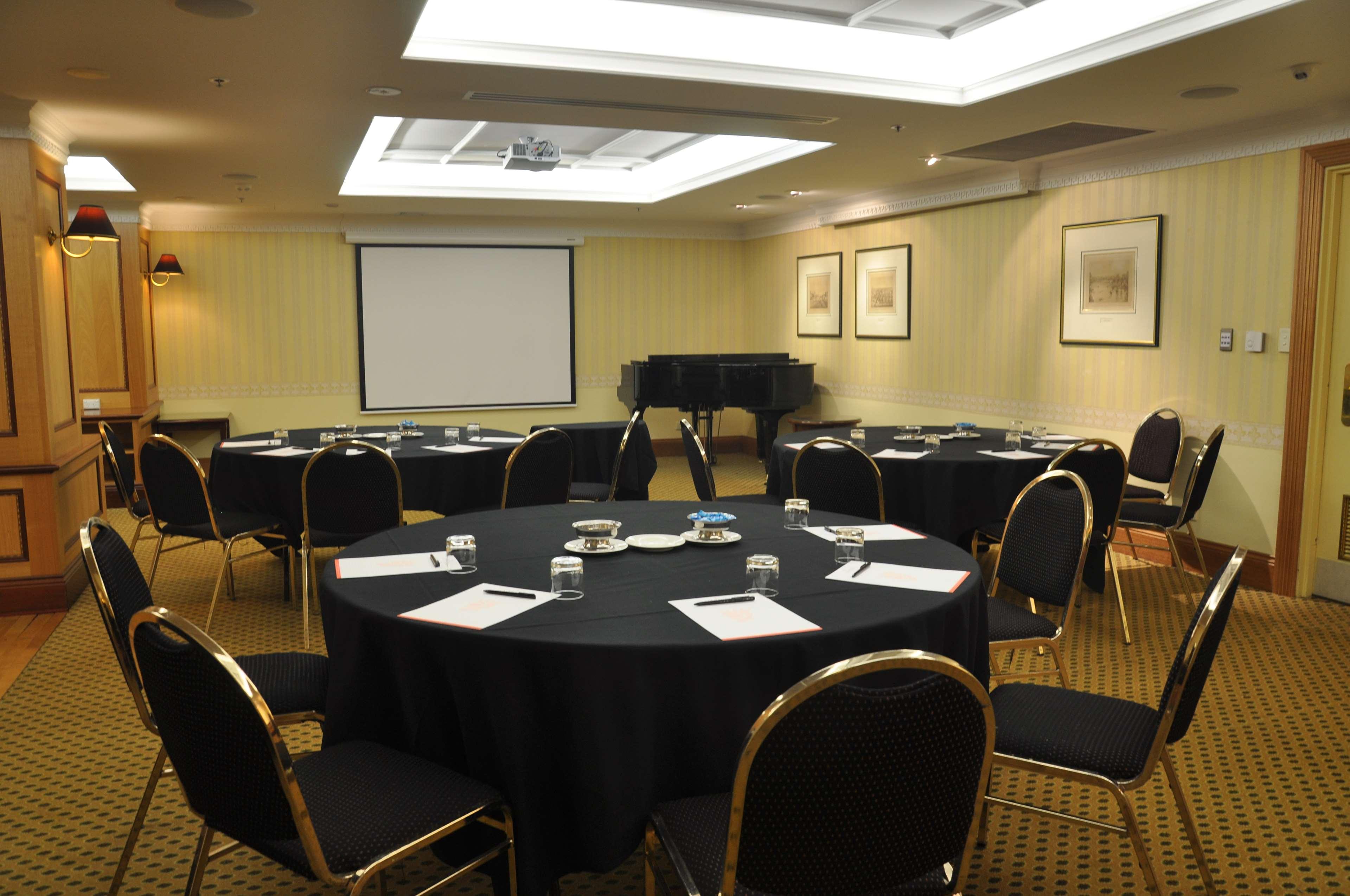 Stamford Plaza Adelaide Hotel Exterior foto The photo shows a conference room set up for a meeting or presentation. There are several round tables covered with black tablecloths, each surrounded by black upholstered chairs. On the tables, there are notepads and glasses of water, indicating tha