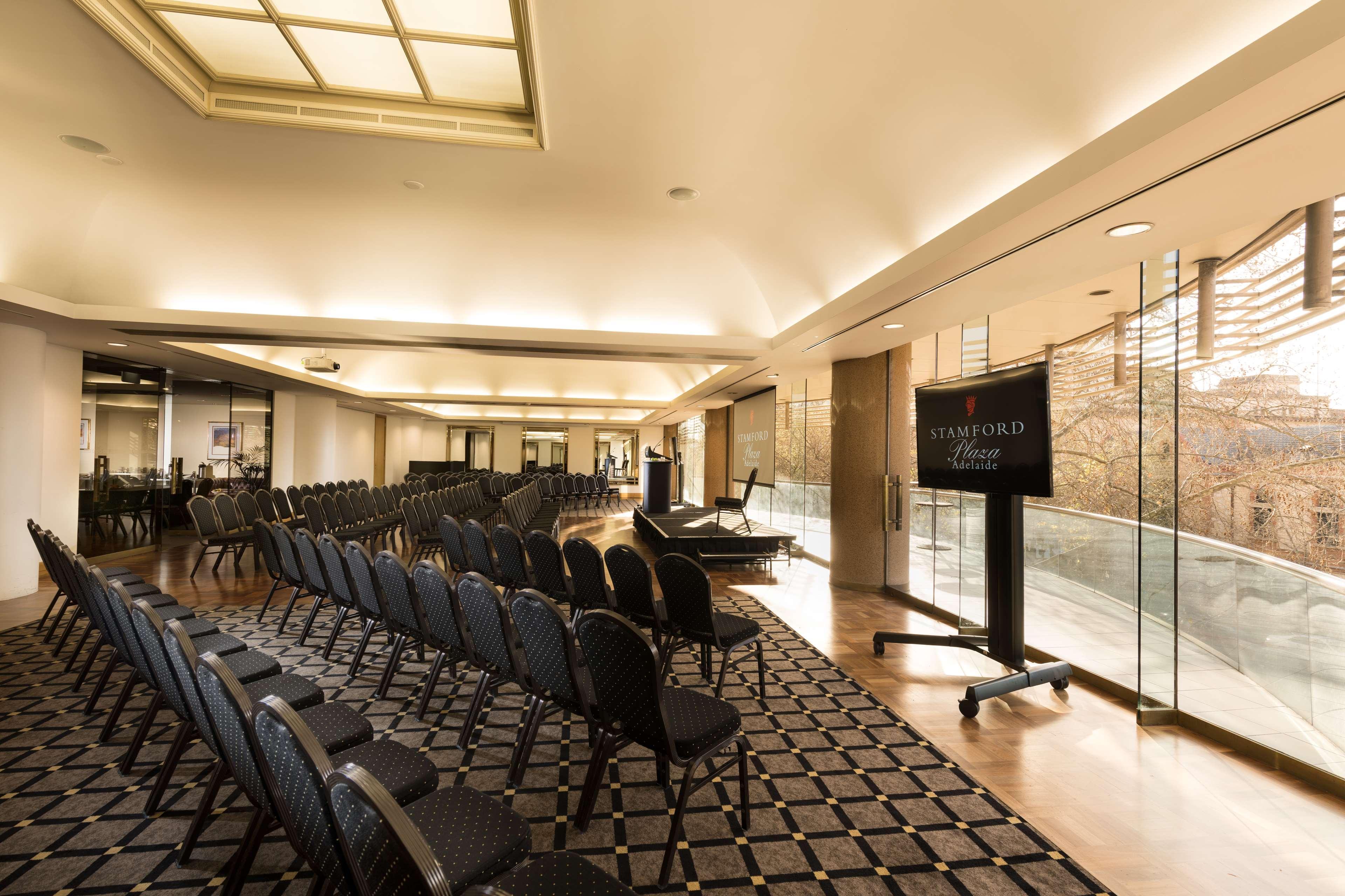 Stamford Plaza Adelaide Hotel Exterior foto The photo shows a large, elegantly designed event space or meeting room. There are rows of black chairs set up facing a presentation area. The flooring features a patterned carpet, and large windows allow natural light to enter the room. On one side,
