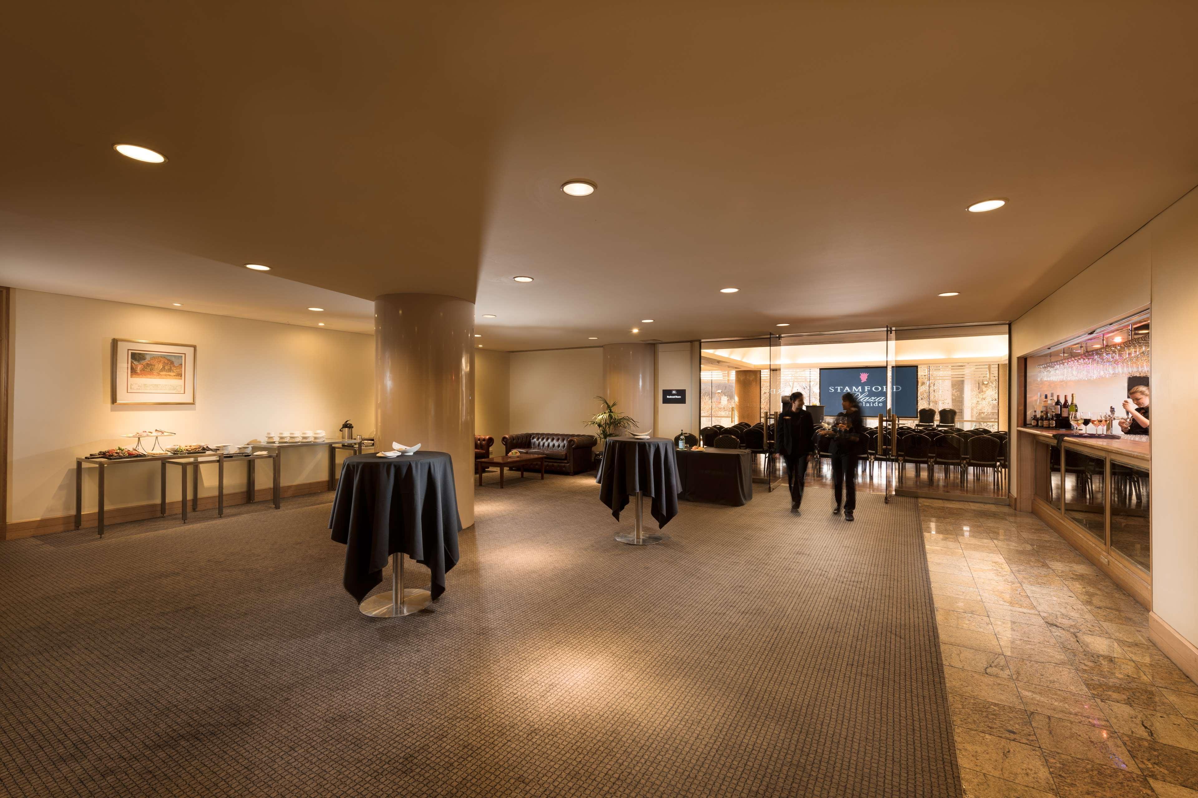 Stamford Plaza Adelaide Hotel Exterior foto The image shows an indoor space that appears to be a lounge or reception area. There are several round tables with dark tablecloths positioned throughout the room. The floor is carpeted, and the lighting is warm and somewhat dim. In the background, t