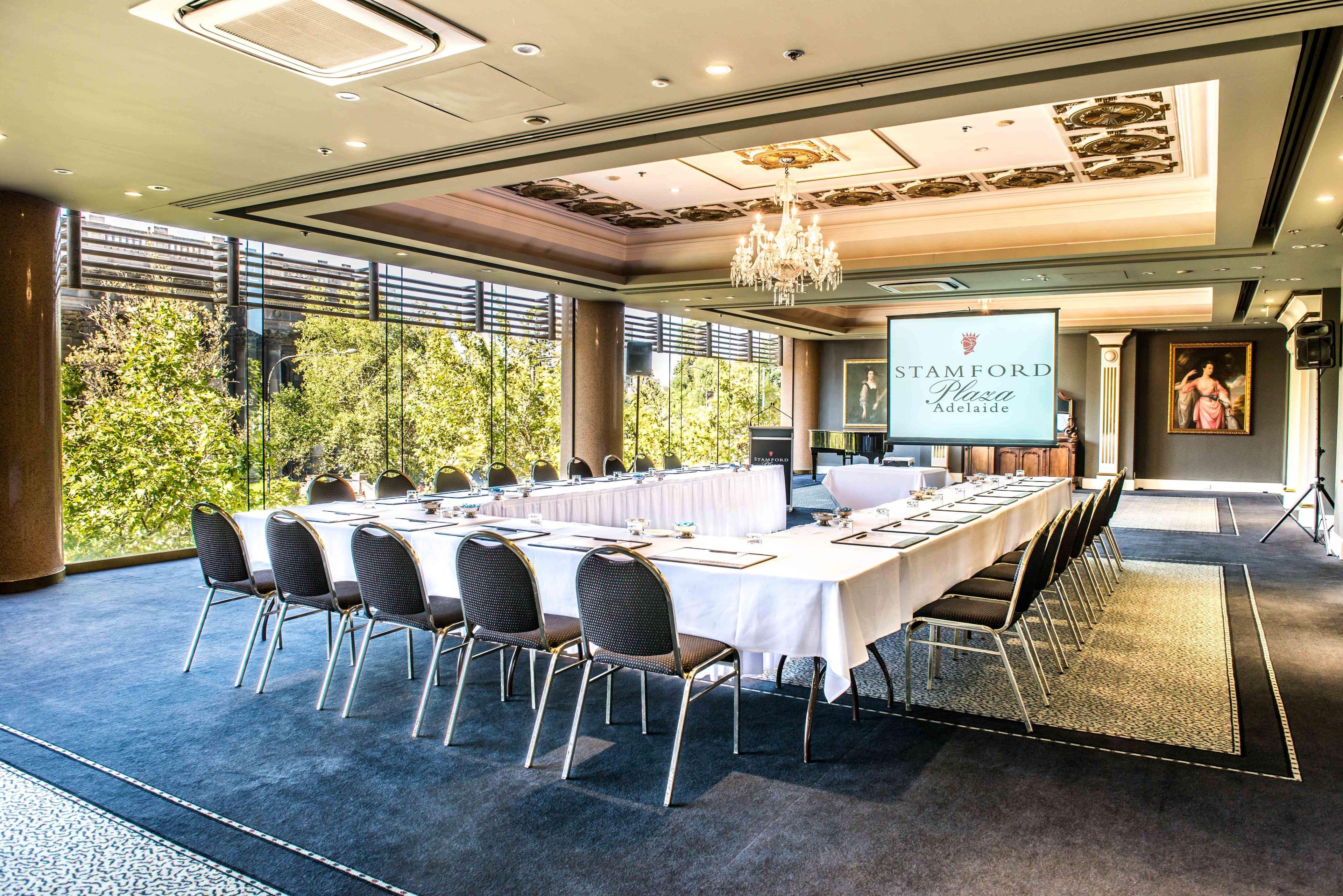 Stamford Plaza Adelaide Hotel Exterior foto The photo shows a stylish conference room set up for a meeting or event. There is a long rectangular table covered with a white tablecloth, surrounded by black chairs. A large screen displays the name "Stamford" along with a logo. The room features l