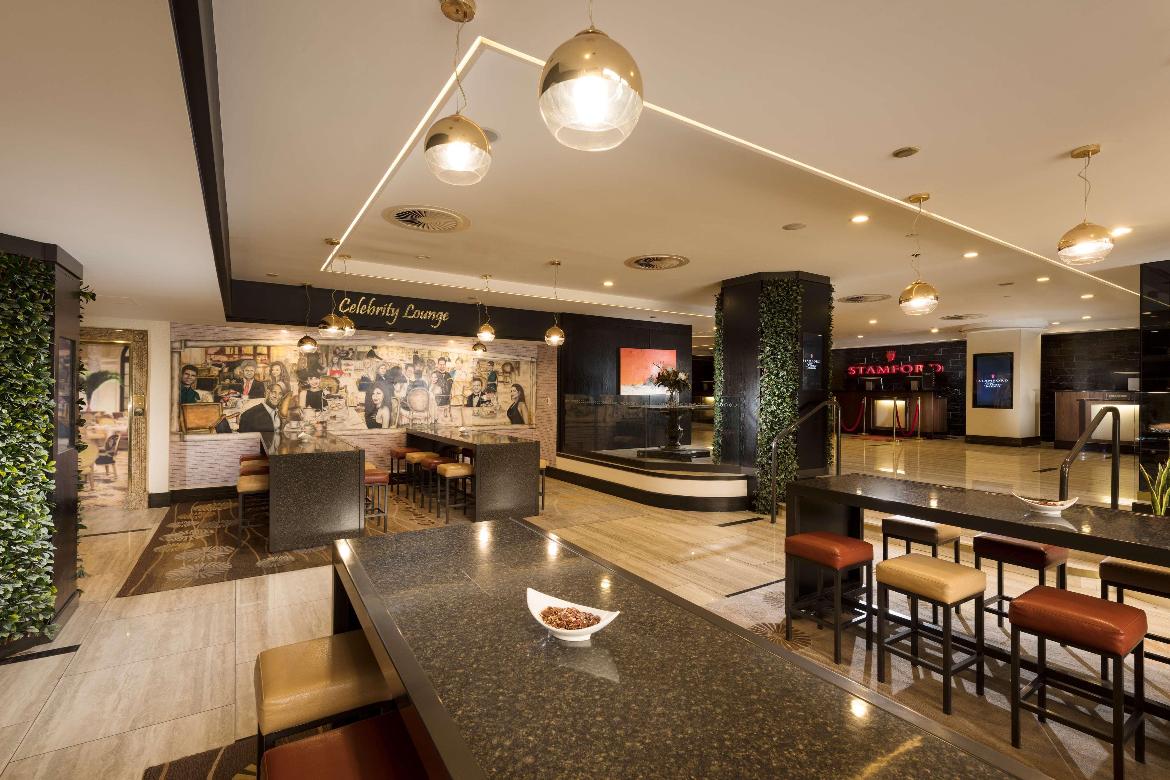Stamford Plaza Adelaide Hotel Exterior foto The photo shows a modern and stylish interior of a lounge or restaurant area. Prominent features include a long dark countertop with bar stools, and several pendant lights hanging from the ceiling. In the background, there is a mural or artwork that 