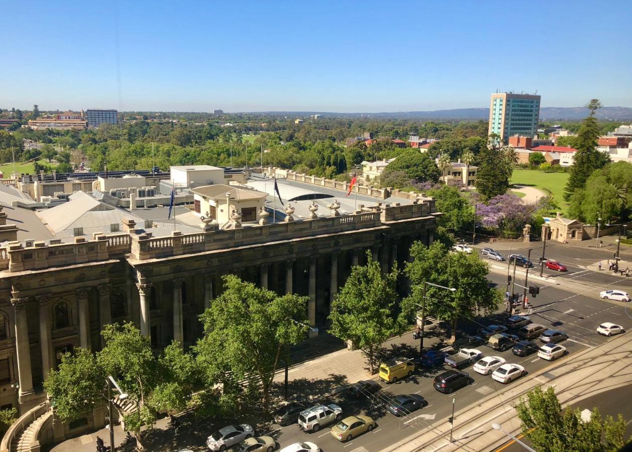 Stamford Plaza Adelaide Hotel Exterior foto The photo depicts a cityscape view, showcasing a mix of architectural structures and greenery. In the foreground, there is a large, classical building with columns, suggesting it may be a historical or governmental structure. Surrounding the building